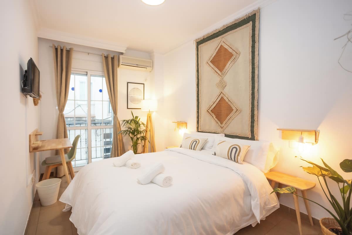 A hotel room with a large bed, a desk, a chair, a TV, and a window with curtains.