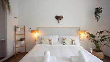 Una cama bien tendida con sábanas y toallas blancas, una escalera de madera y una planta en la pared.
