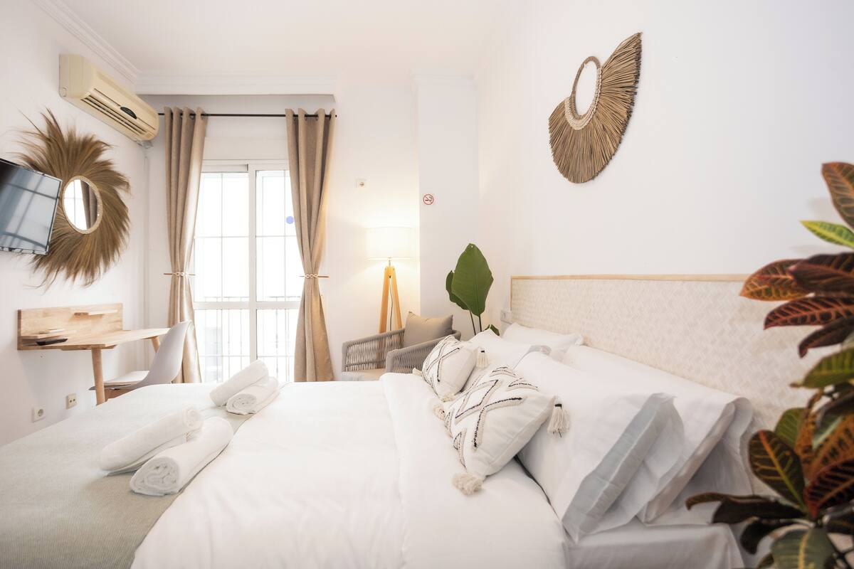 A hotel room with a bed, a desk, a chair, a TV, and a large window with curtains.