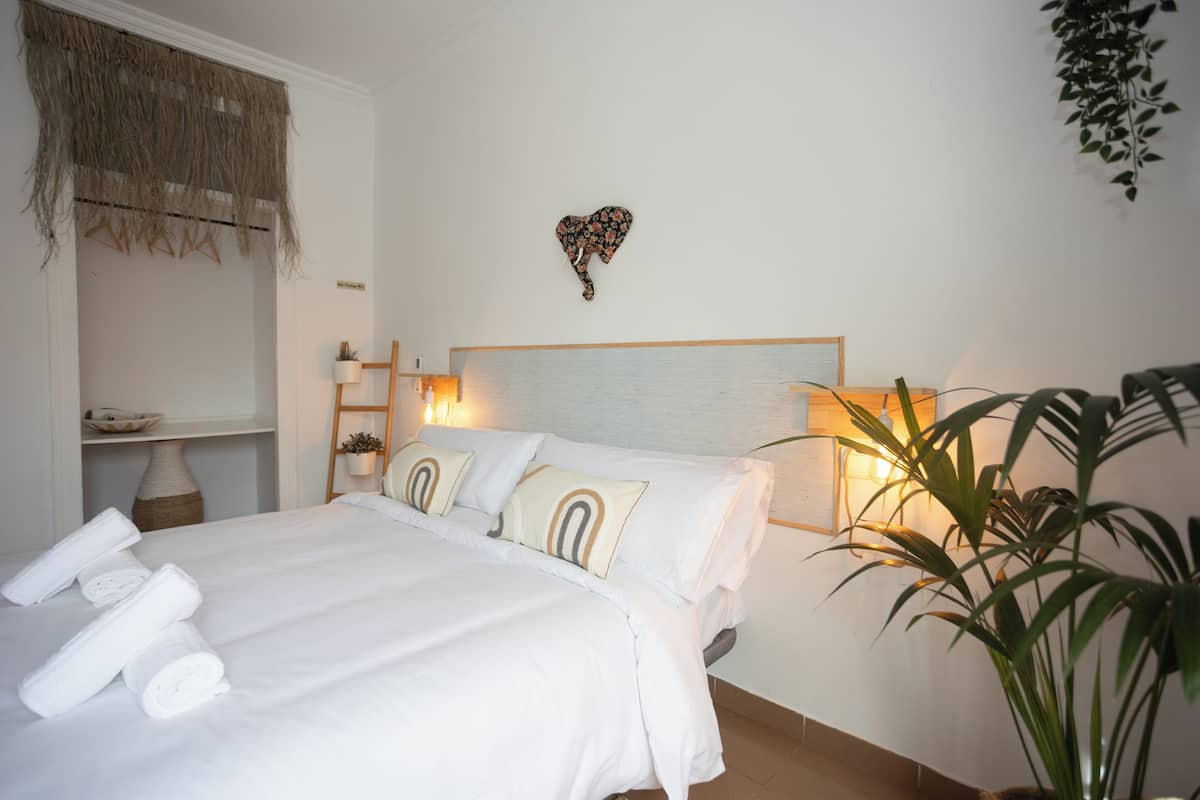 A neatly made bed with white linens and decorative pillows, a bedside table with a lamp, and a wall-mounted heart-shaped decoration.