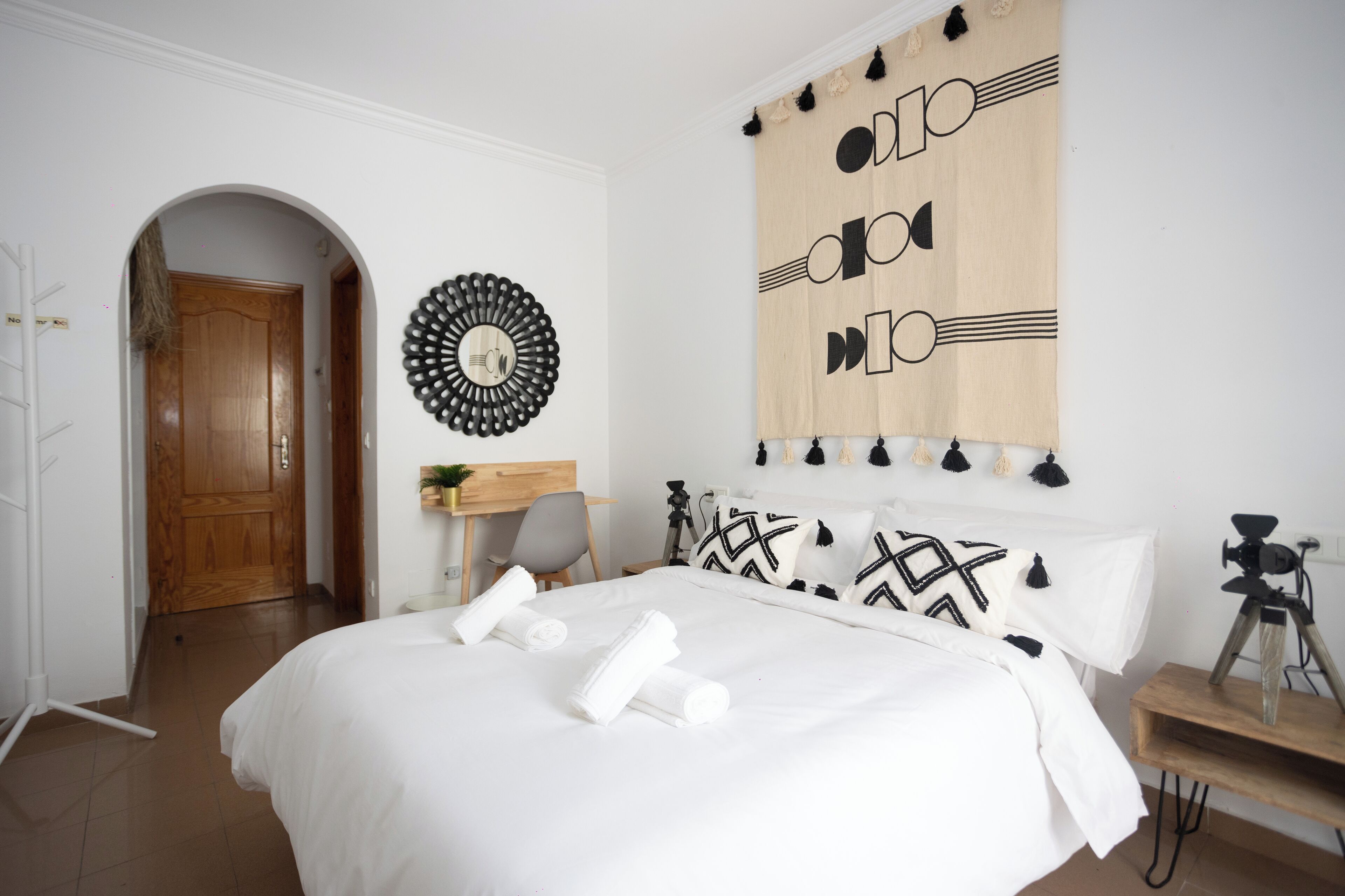 A bedroom with a bed, a desk, and a camera on a tripod.