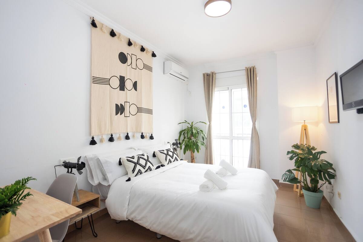 A hotel room with a bed, a desk, a chair, a potted plant, and a TV on the wall.