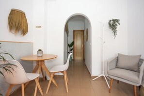 A modern living room with a round wooden table, white chairs, a grey sofa, and a hanging plant. - Naim Guest House Nerja (Nerja)