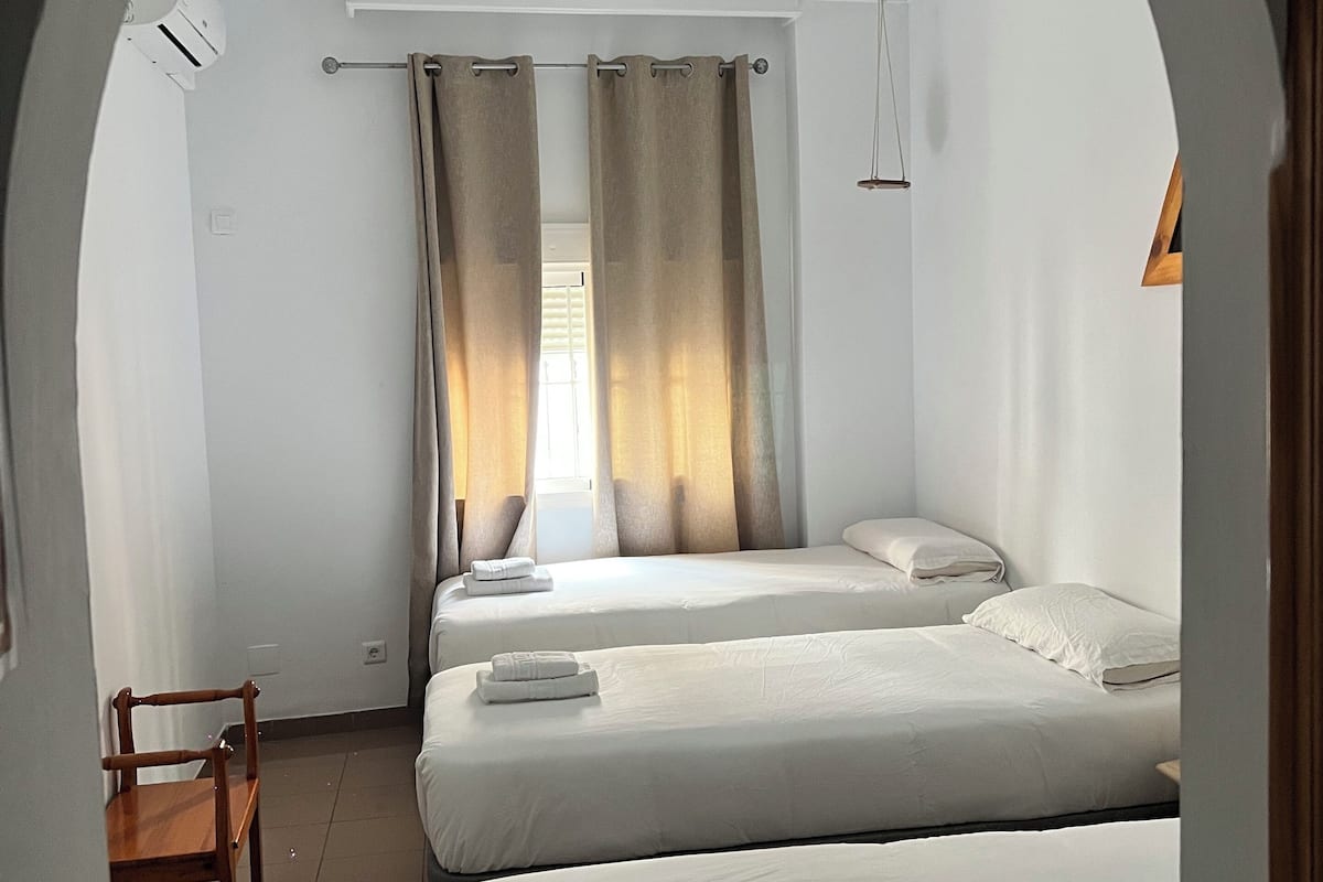 A hotel room with two beds, a wooden chair, and a window with curtains.