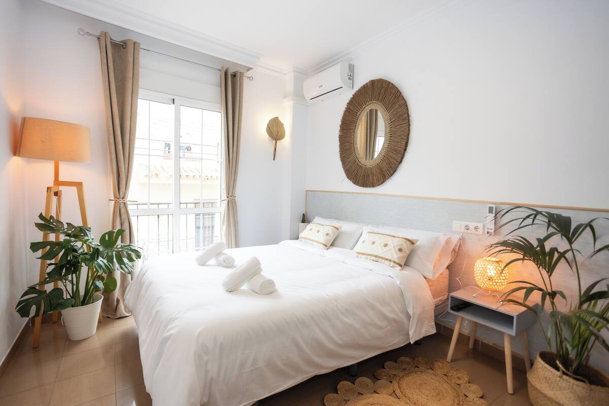 A hotel room with a large bed, a bedside lamp, a potted plant, and a wall-mounted mirror.