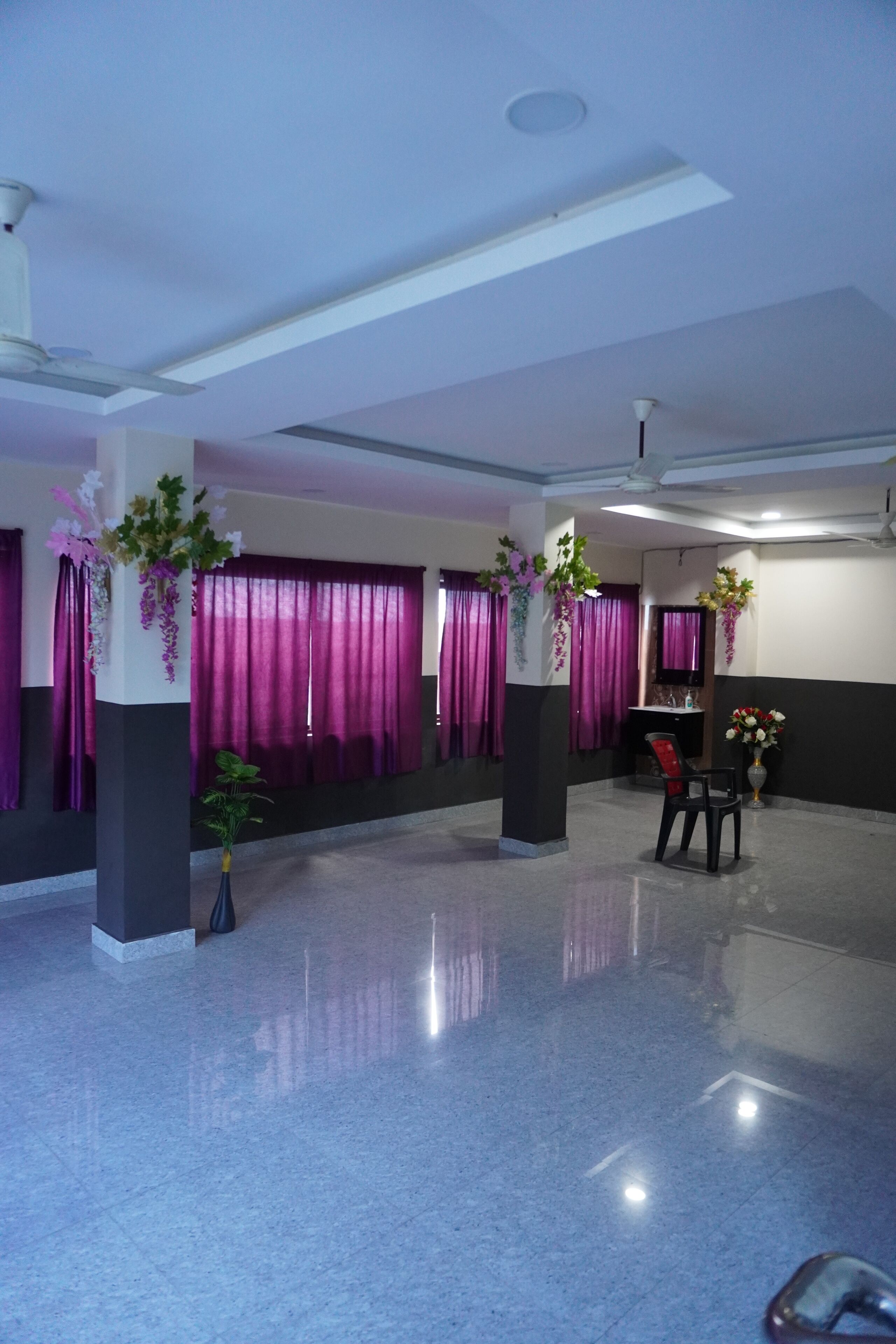 A spacious lobby with a polished floor, purple curtains, and decorative plants.