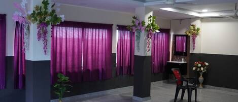 A spacious lobby with a polished floor, purple curtains, and decorative plants.