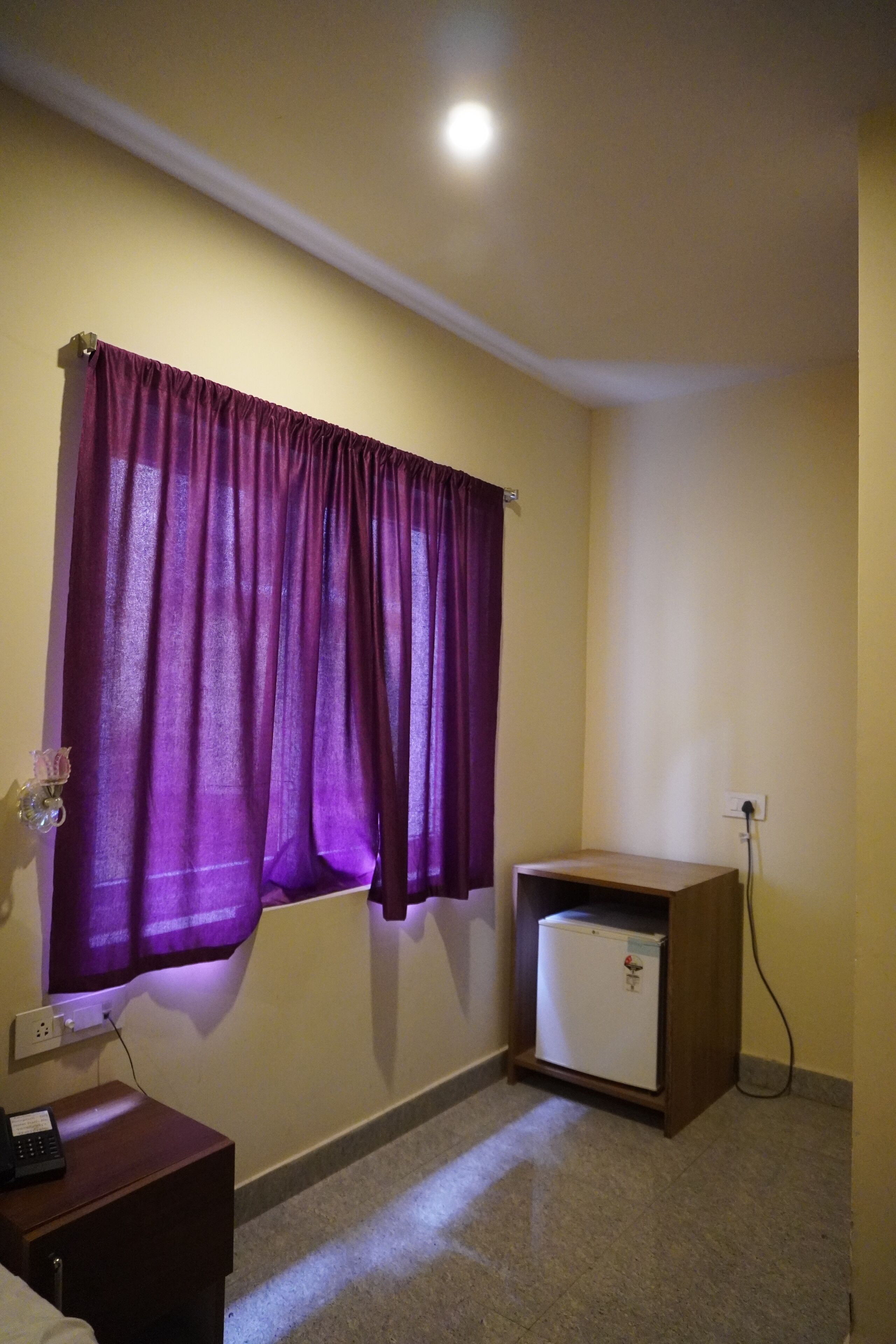 Una habitación pequeña con una cortina morada, un mueble de madera pequeño y un refrigerador blanco.