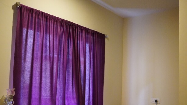 Una habitación pequeña con una cortina morada, un mueble de madera pequeño y un refrigerador blanco.