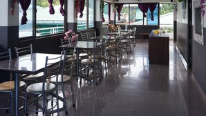 A restaurant with multiple tables and chairs, ceiling fans, and large windows with curtains. - NS RESIDENCY (Port Blair)