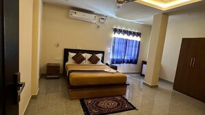 A hotel room with a bed, a ceiling fan, an air conditioning unit, a window with curtains, and a wooden wardrobe. - NS RESIDENCY (Port Blair)