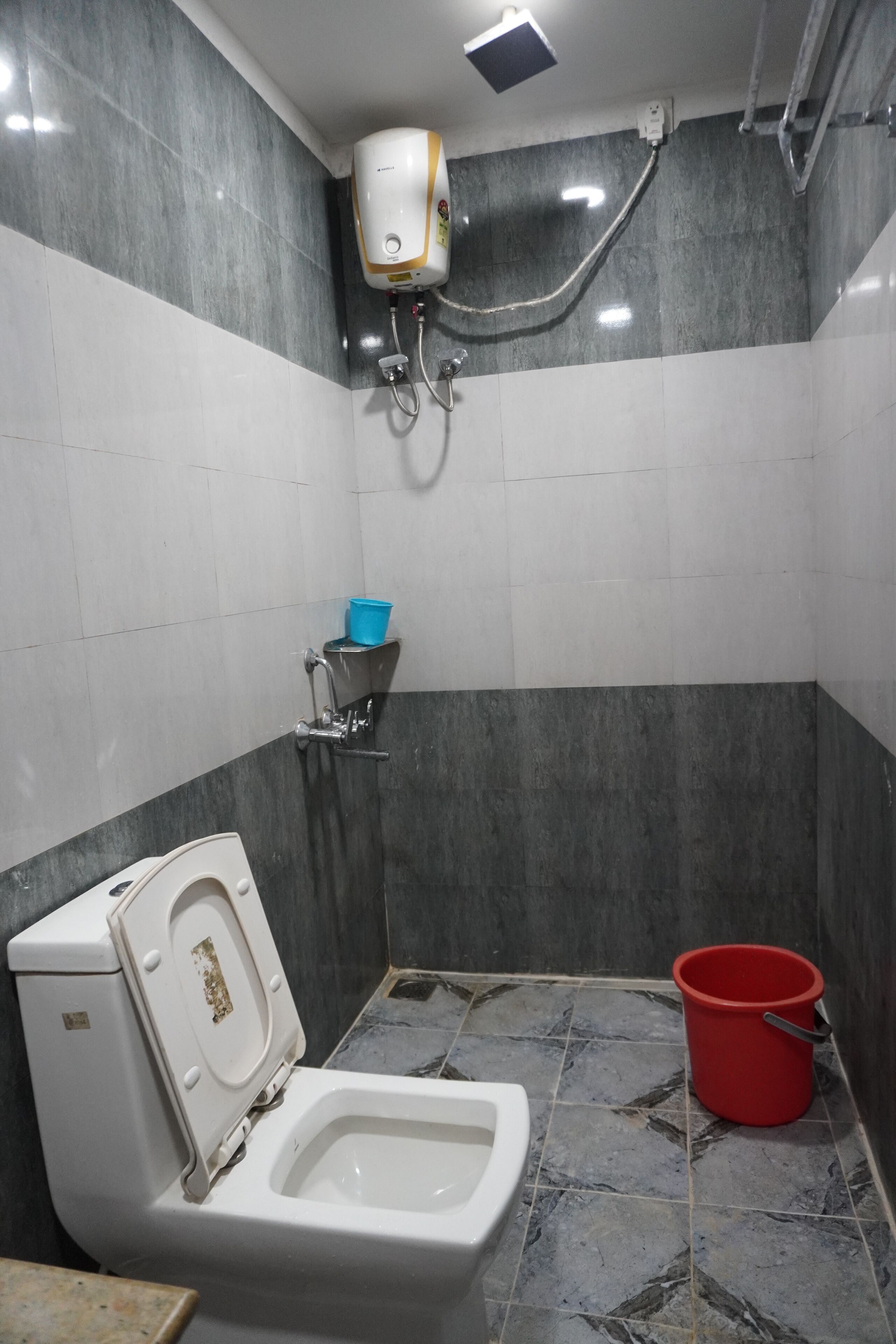 Une salle de bain équipée de toilettes, d’un sèche-mains et d’un seau rouge.