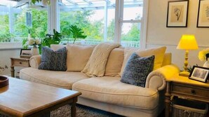 A cozy living room with a beige sofa, a wooden coffee table, and a yellow lamp. - The Hollies (Monbulk)