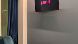 A room with a flat-screen TV mounted on the wall displaying the Netflix logo, a blue sofa, and a small round table. - Serendipity Rooms - Navigli (Milan)