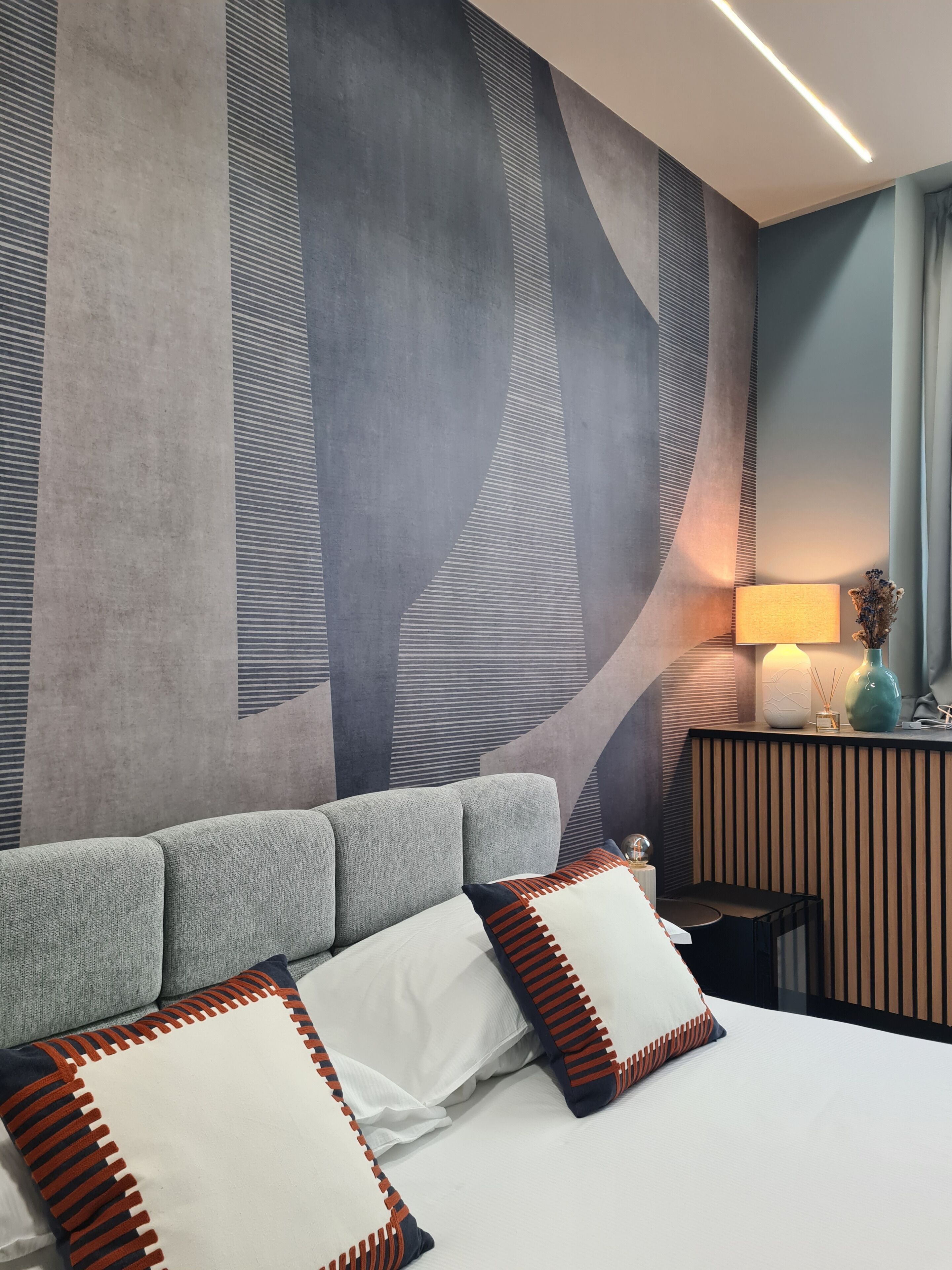 Une chambre d’hôtel moderne avec un grand lit, un bureau avec une lampe et un mur décoratif.