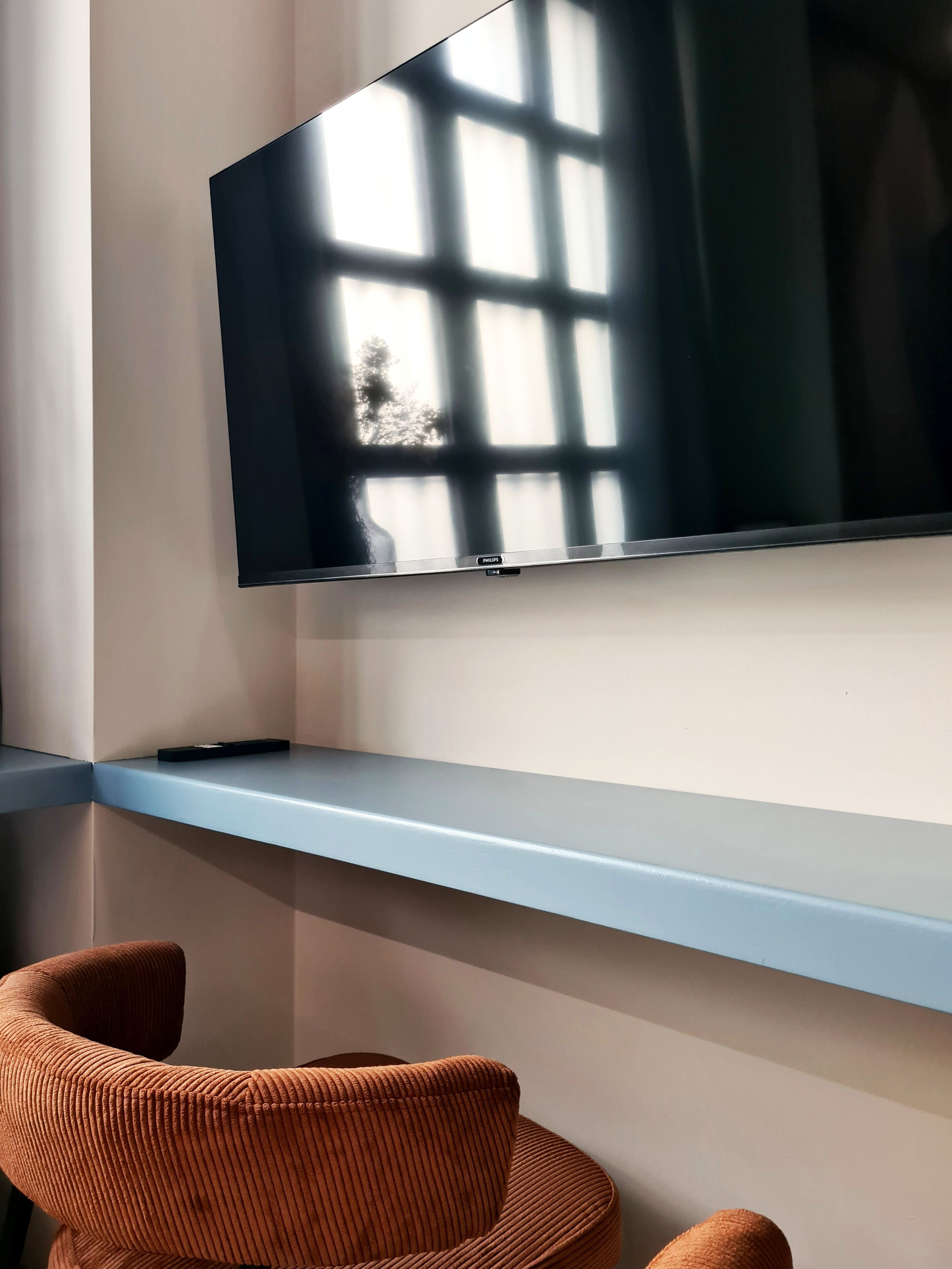 A modern room with a flat-screen TV mounted on a wall, a blue shelf below it, and a brown chair.