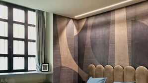 A modern bedroom with a bed, a chair, a window, and a wall with a geometric pattern. - Serendipity Rooms - Navigli (Milan)