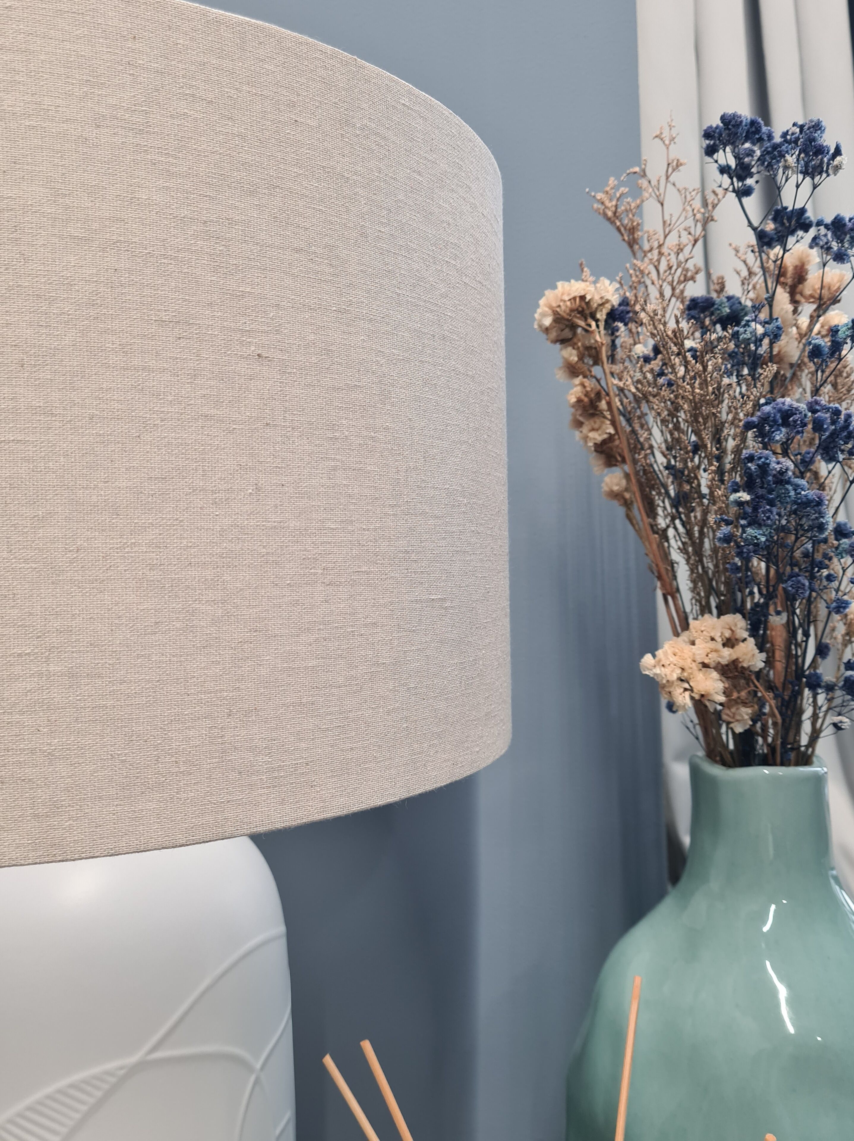 Une pièce avec un grand mur beige à la texture marquée, un canapé blanc à la texture similaire et un vase vert contenant des fleurs séchées.