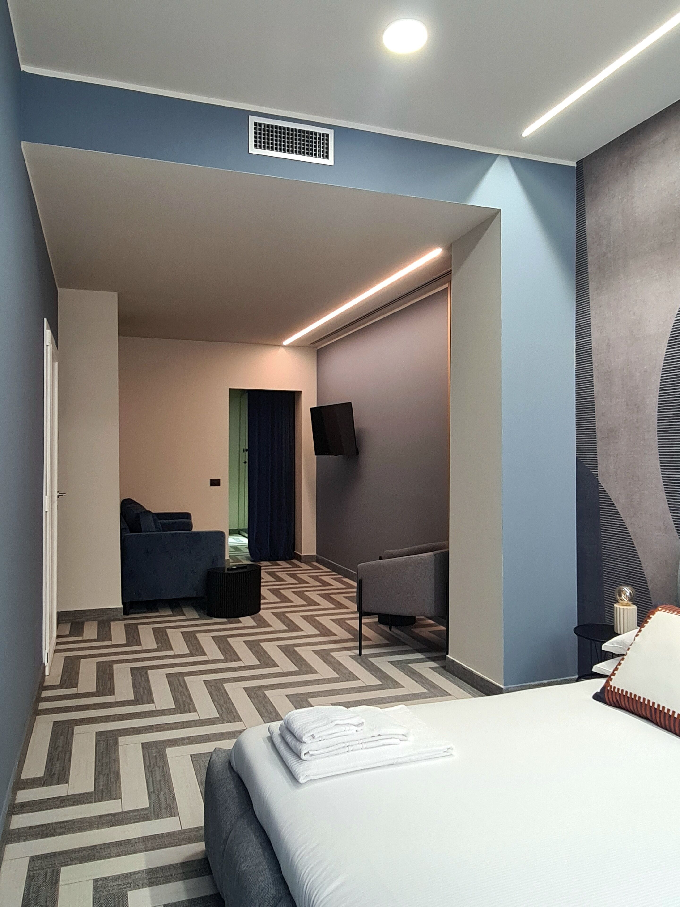 Une chambre d’hôtel moderne dotée d’un grand lit, de deux coins salon, d’un téléviseur à écran plat et d’une moquette à motifs.