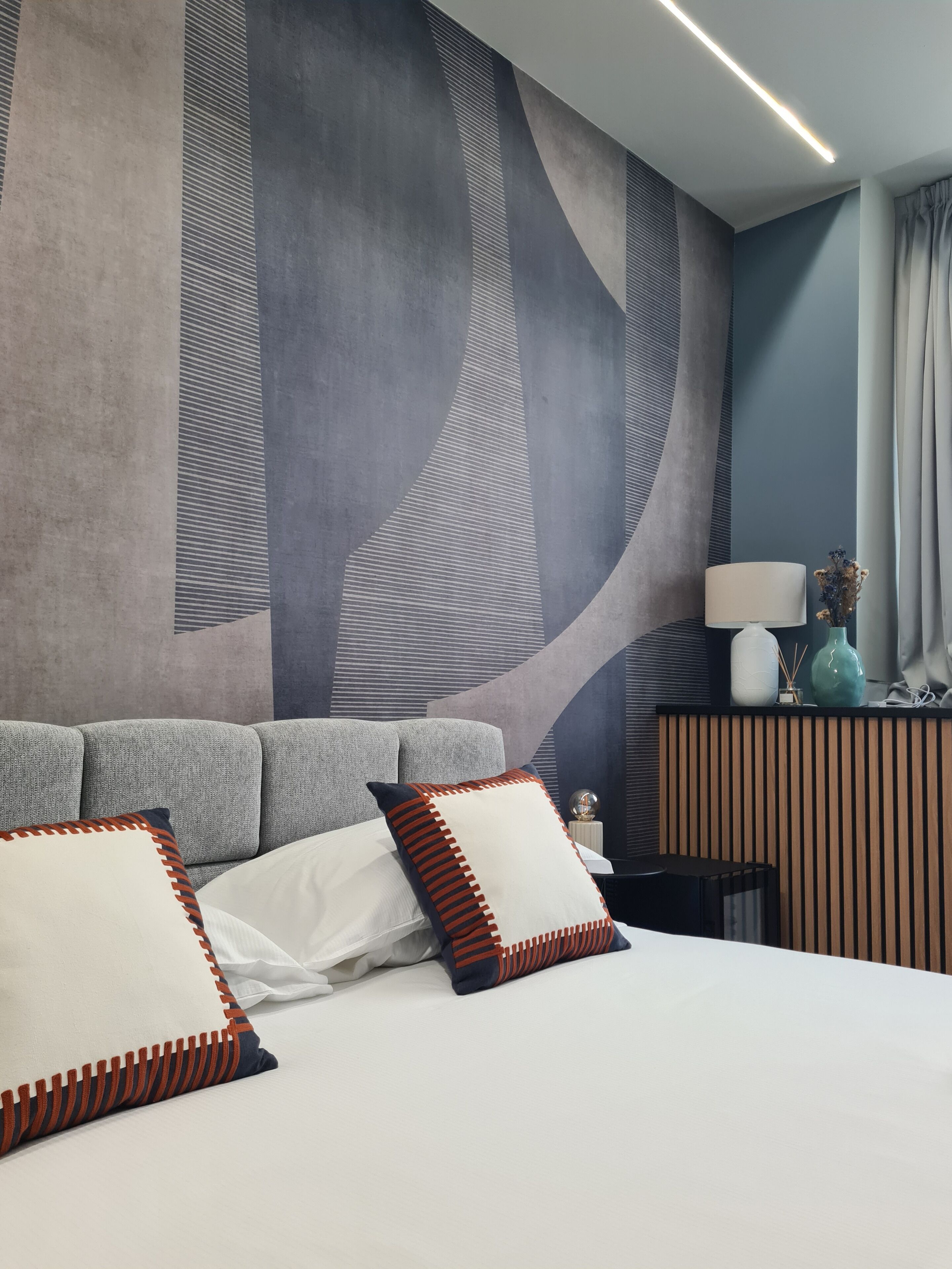 A modern hotel room with a large bed, a sofa, a nightstand, and a wall with abstract art.