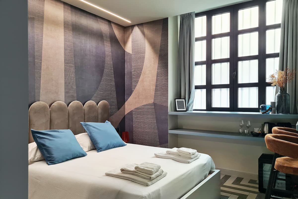 A modern bedroom with a bed, pillows, a desk, and a window with curtains.