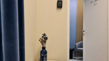 A hotel room with a door marked "no suite 02", a small table with a vase of flowers, and a blue curtain.