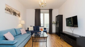 Ein Wohnzimmer mit blauem Sofa, Couchtisch, Fernseher und Schrank.