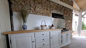 Una cocina con pared de piedra, armarios blancos y encimera de madera.