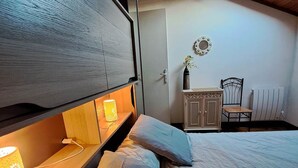 Un dormitorio con literas, un escritorio con silla, un radiador y un tragaluz.