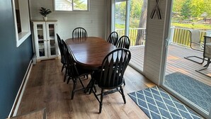 Un comedor con mesa y sillas de madera, un armario con puertas de vidrio y vista a una terraza por medio de puertas de cristal.