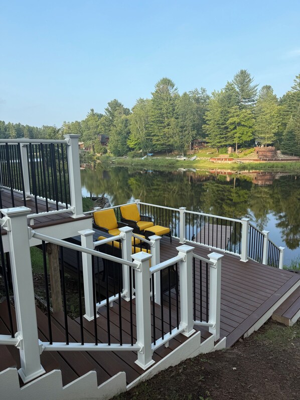 A deck with outdoor seating overlooking a calm lake, surrounded by trees.