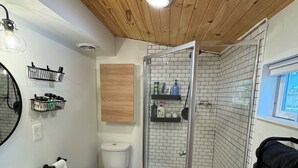 A bathroom with a white toilet, a glass-enclosed shower, a white sink, and a wooden ceiling.
