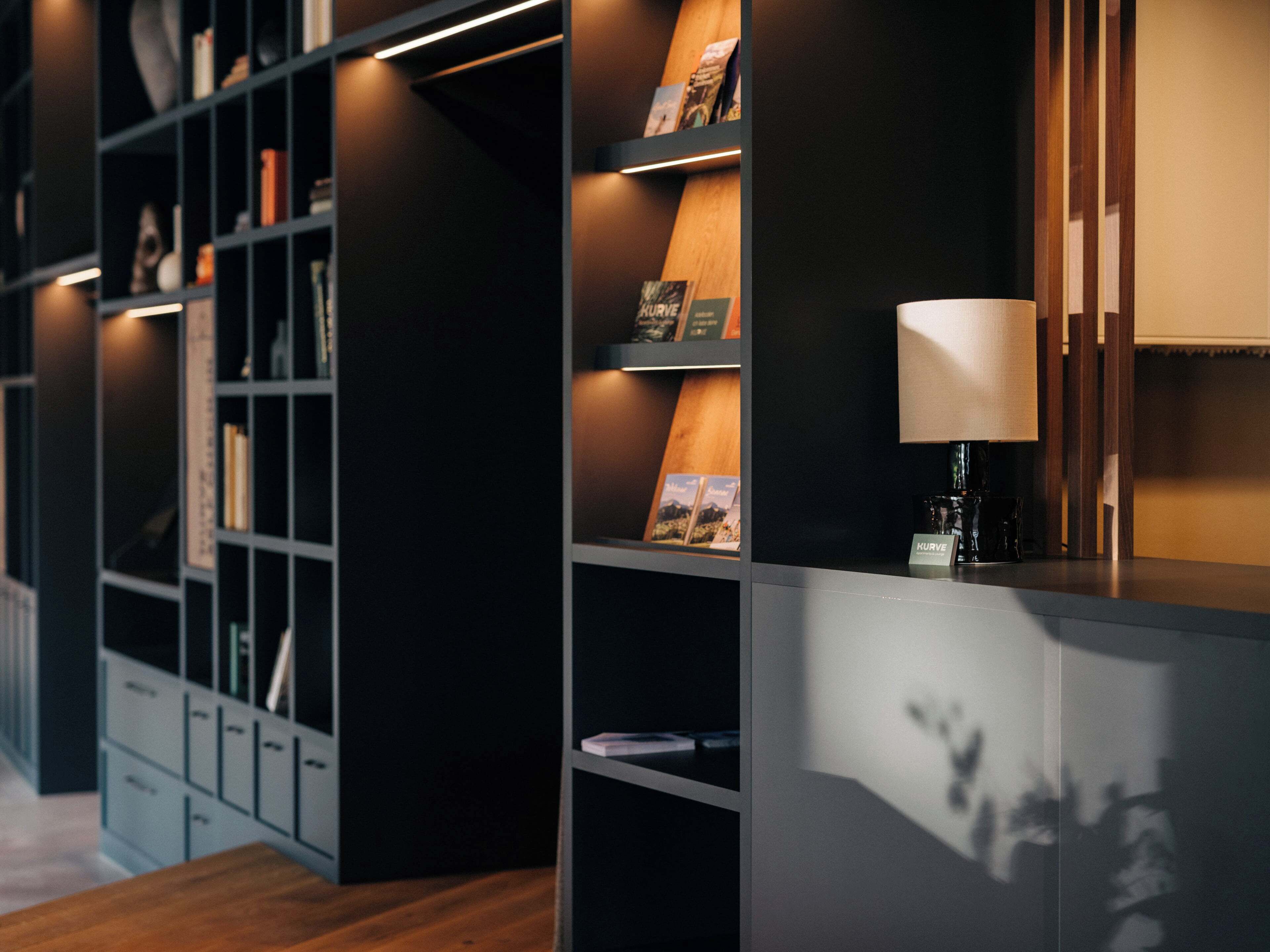Eine moderne Bibliothek mit Bücherregalen, einer Kaffeemaschine und einer Lampe.