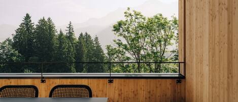 Ein modernes Zimmer mit Holzboden, einem Tisch und zwei Stühlen. Es bietet ein großes Fenster mit Blick auf Bäume und Berge.