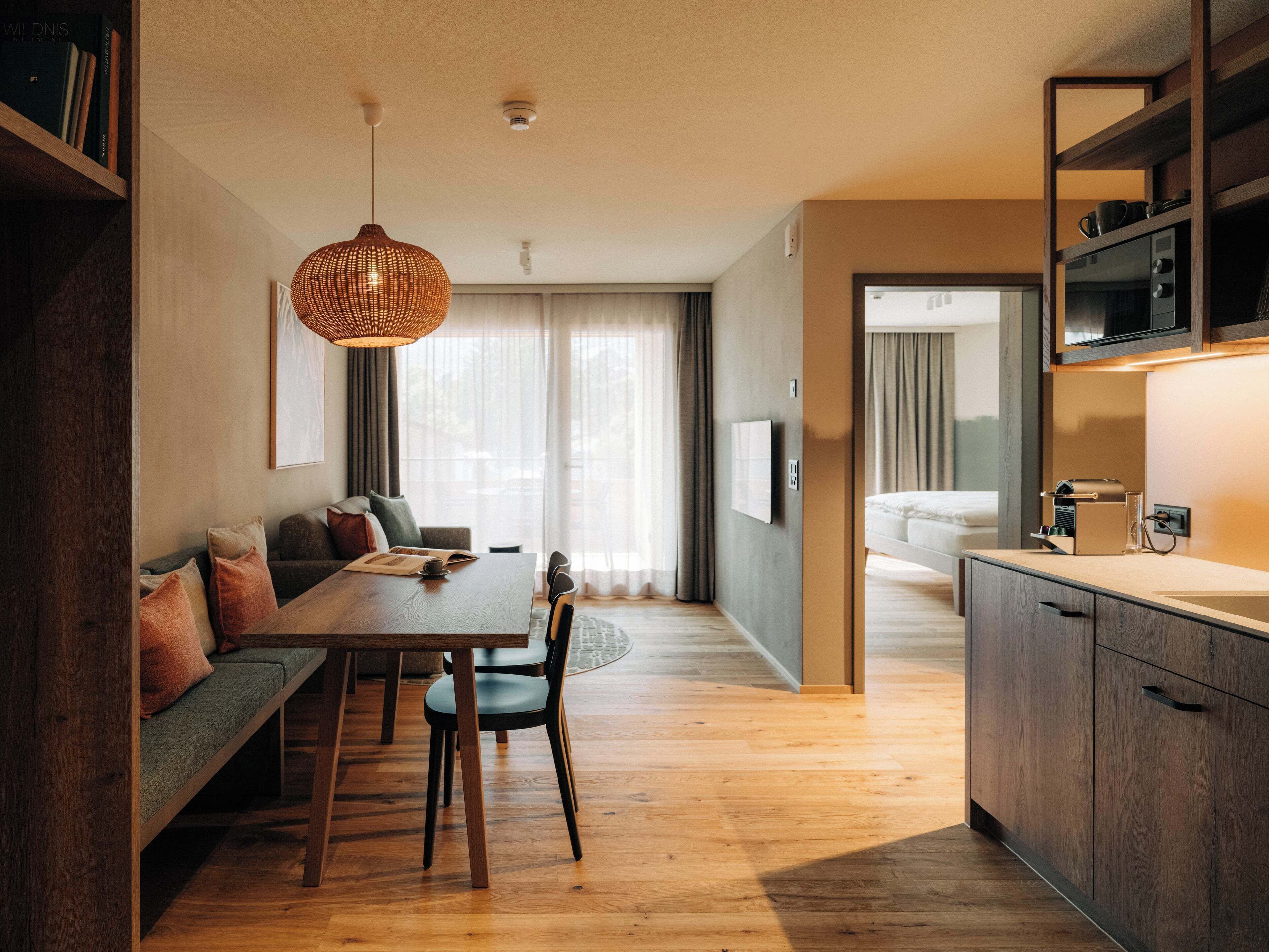 A modern kitchen with wooden cabinets, a dining area with a wooden table and chairs, and a large window with curtains.