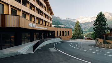 A modern building with a wooden facade, labeled "KURVE Apartments & Lounge," featuring a curved driveway and a mountain backdrop.