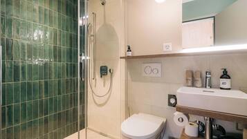 A modern bathroom with a glass-enclosed shower, a toilet, and a sink with toiletries.