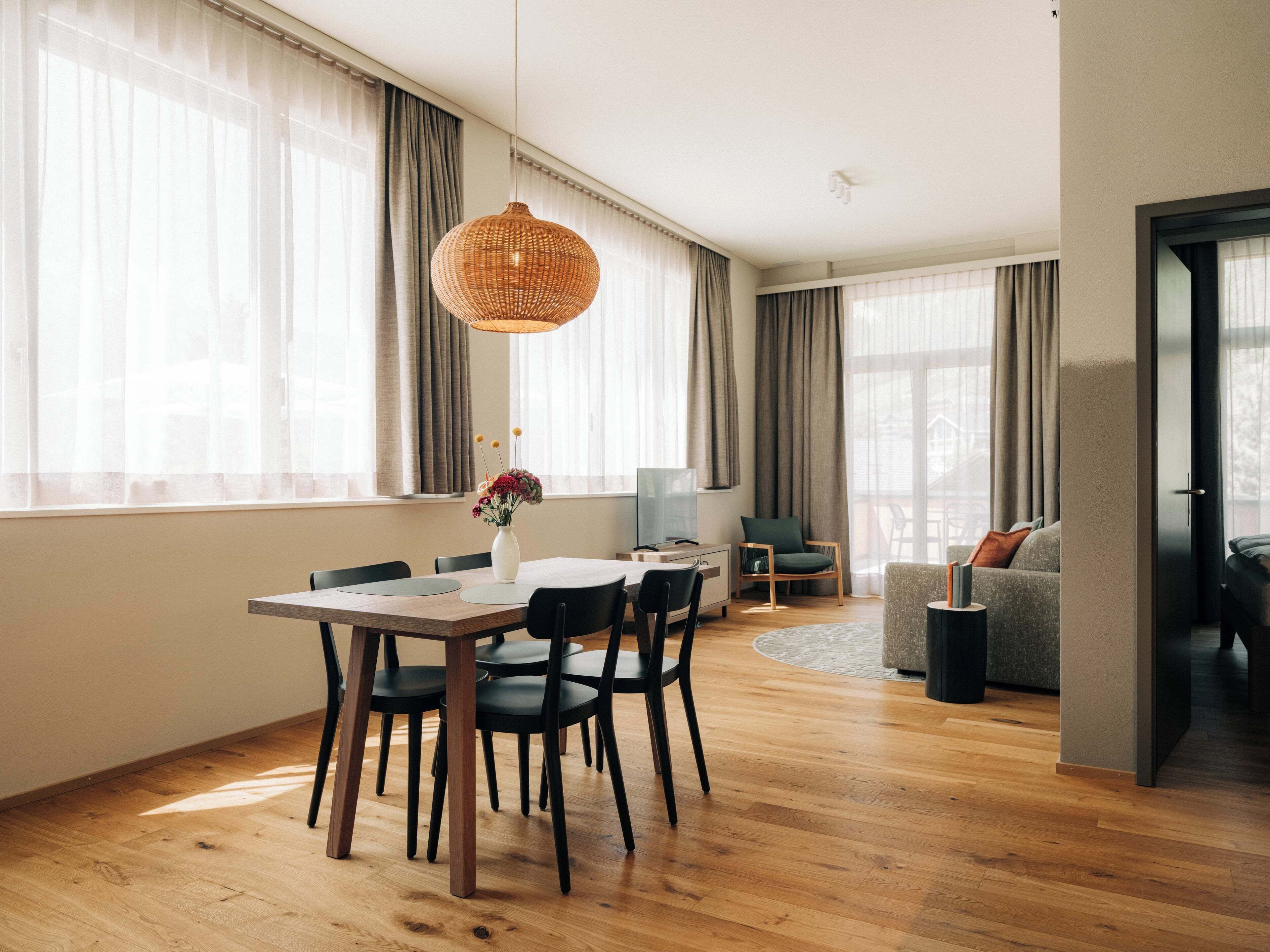 Ein zeitgemäßer Wohnbereich mit Essbereich, einer Couch und einem großen Fenster mit Vorhängen.