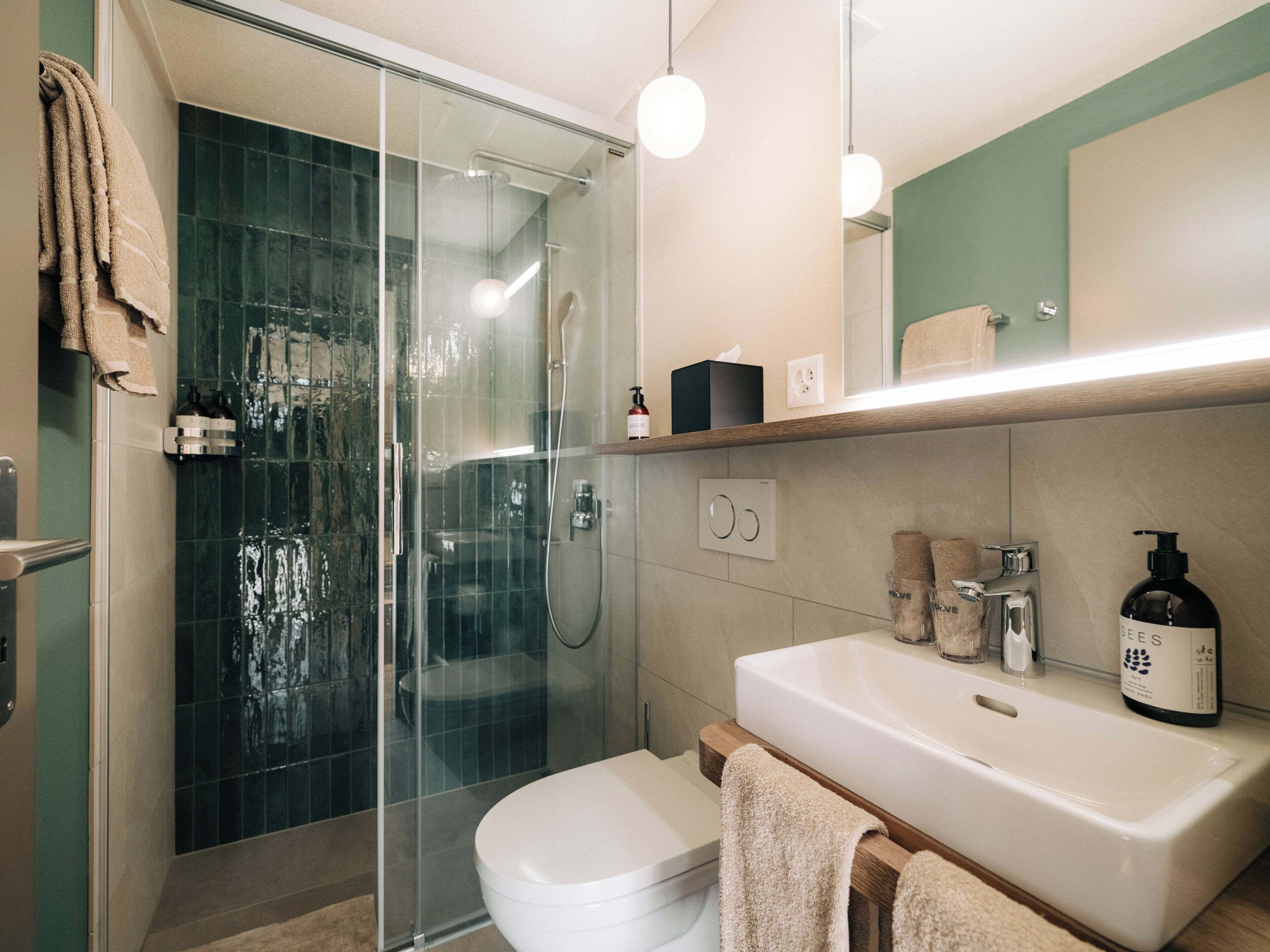 Un bagno moderno con box doccia in vetro, un water bianco, un lavabo con piano in legno e uno specchio sopra il lavabo.