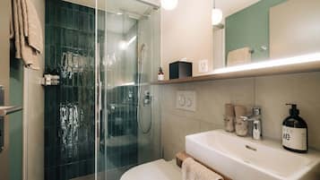 Un bagno moderno con box doccia in vetro, un water bianco, un lavabo con piano in legno e uno specchio sopra il lavabo.