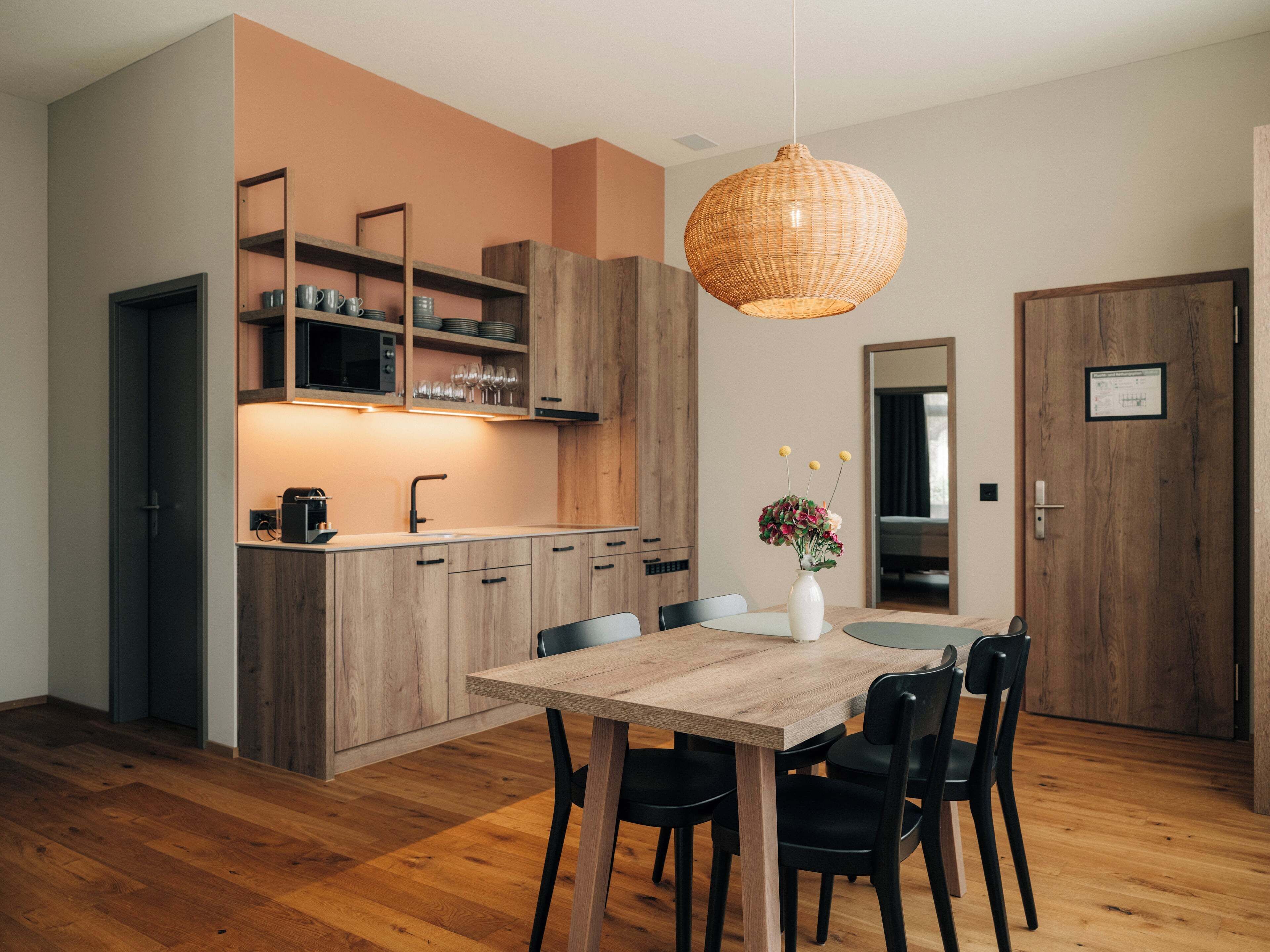 A modern kitchen with wooden cabinets, a dining table with chairs, and a hanging light fixture.