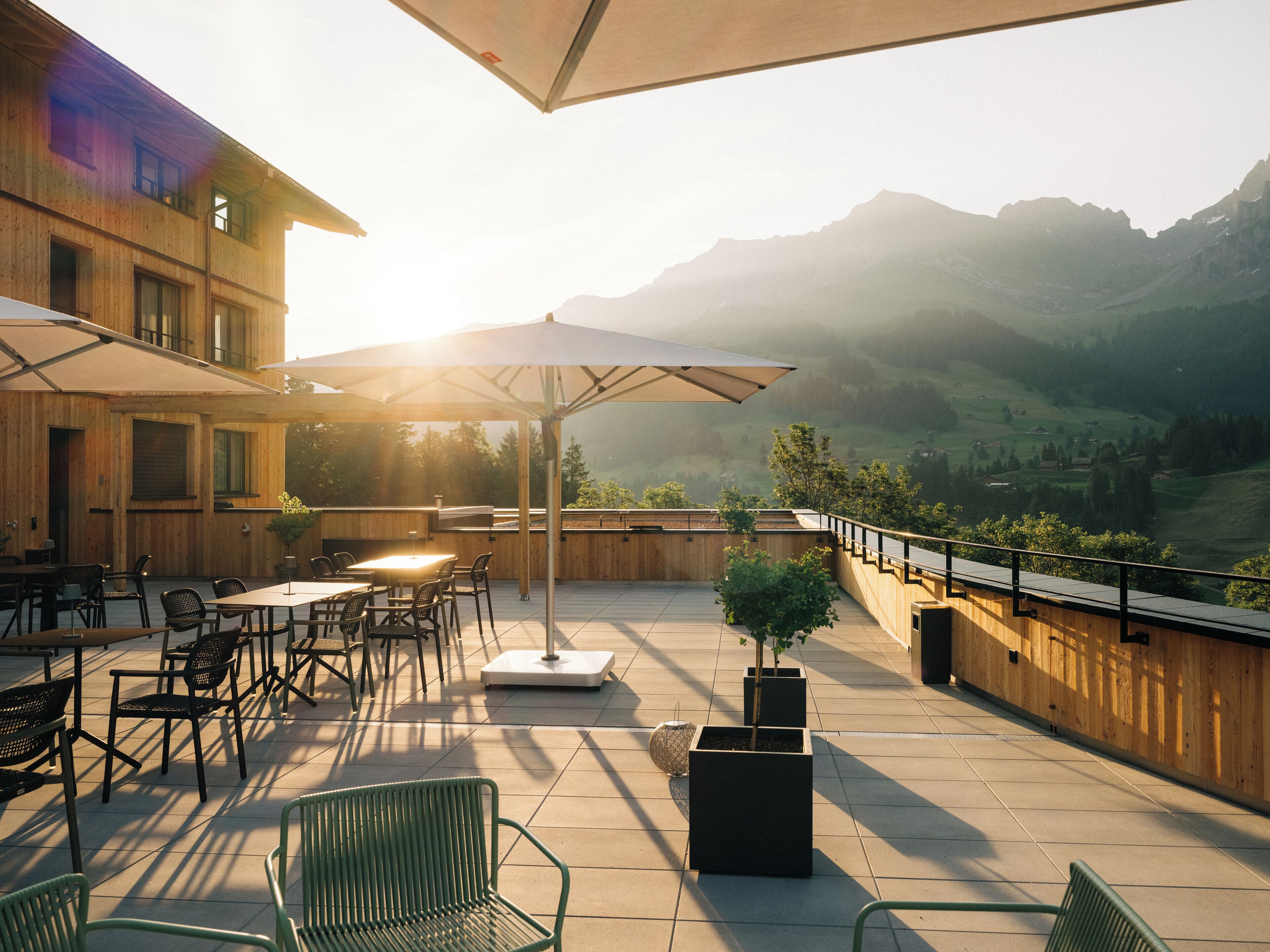 An outdoor patio with tables and chairs, surrounded by wooden walls and a view of mountains.