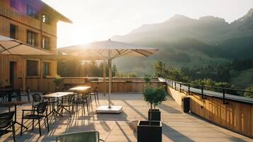 An outdoor patio with tables and chairs, surrounded by wooden walls and a view of mountains.