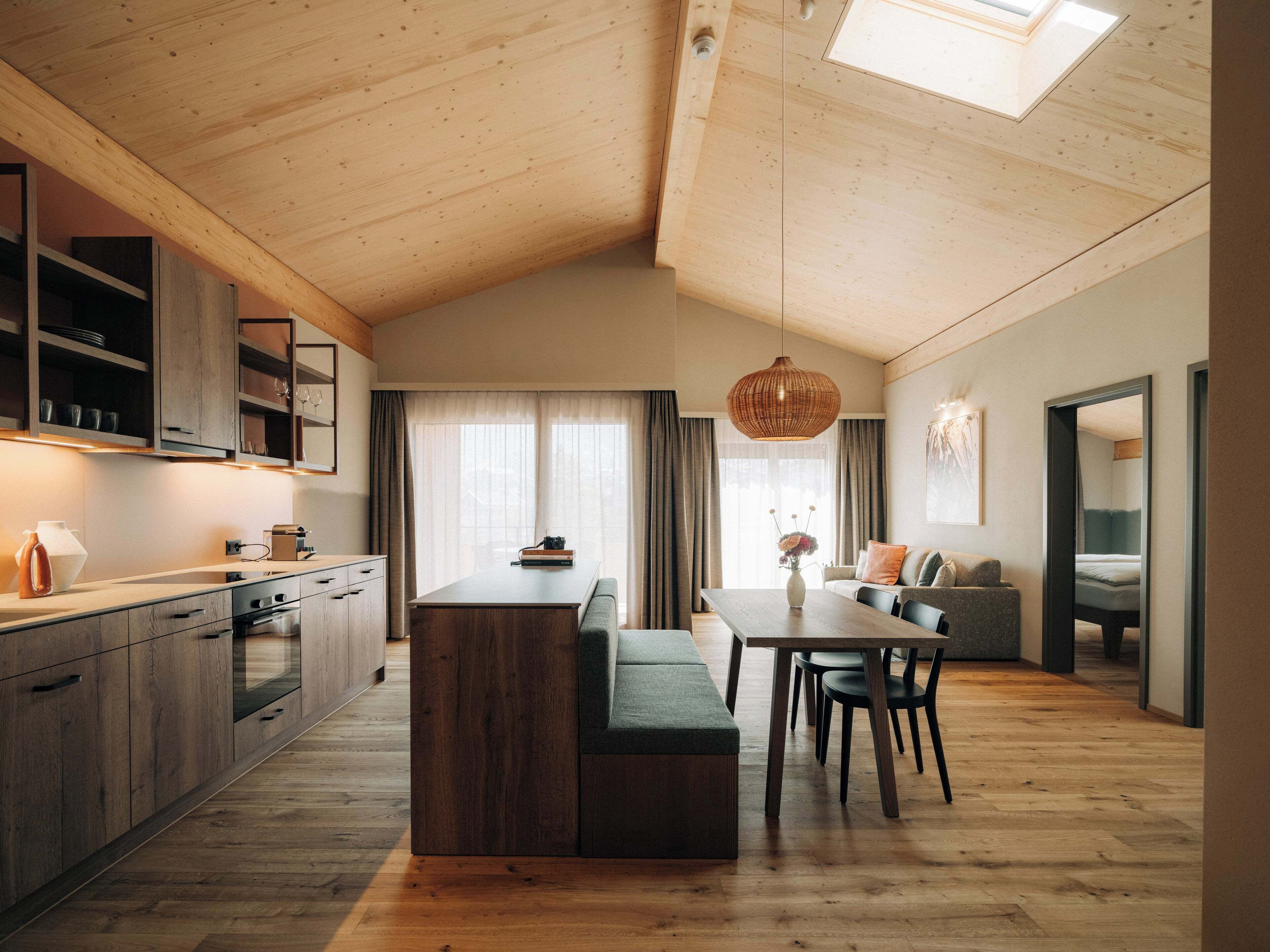 A modern kitchen with wooden cabinets, a dining area with a table and chairs, and a cozy seating area with a sofa and cushions.