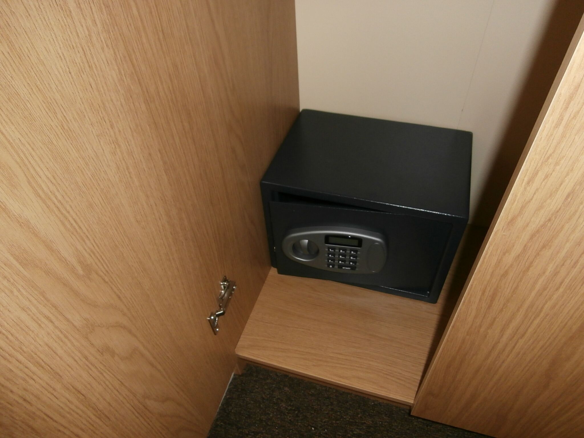 A small, black safe with a keypad, mounted on a wooden cabinet in a corner.