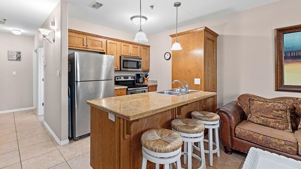 A modern kitchen with a central island, stainless steel appliances, wooden cabinets, and a brown leather sofa in the living area. - Marlin by South Padre Resort Rentals (South Padre Island)