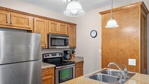A kitchen with wooden cabinets, stainless steel appliances, granite countertops, and pendant lighting. - Marlin by South Padre Resort Rentals (South Padre Island)