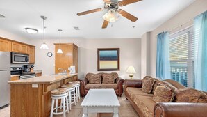 A modern kitchen with a central island, bar stools, a white coffee table, and a brown leather sofa. - Marlin by South Padre Resort Rentals (South Padre Island)