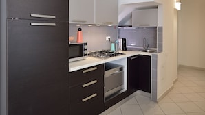 A modern kitchen with dark cabinetry, a gas stove, a microwave, and a sink. - Mina Suite - Double Apartment (Cattolica)
