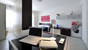 A modern hotel room with a desk, laptop, notebook, and a bed in the background. - Mina Suite - Double Apartment (Cattolica)